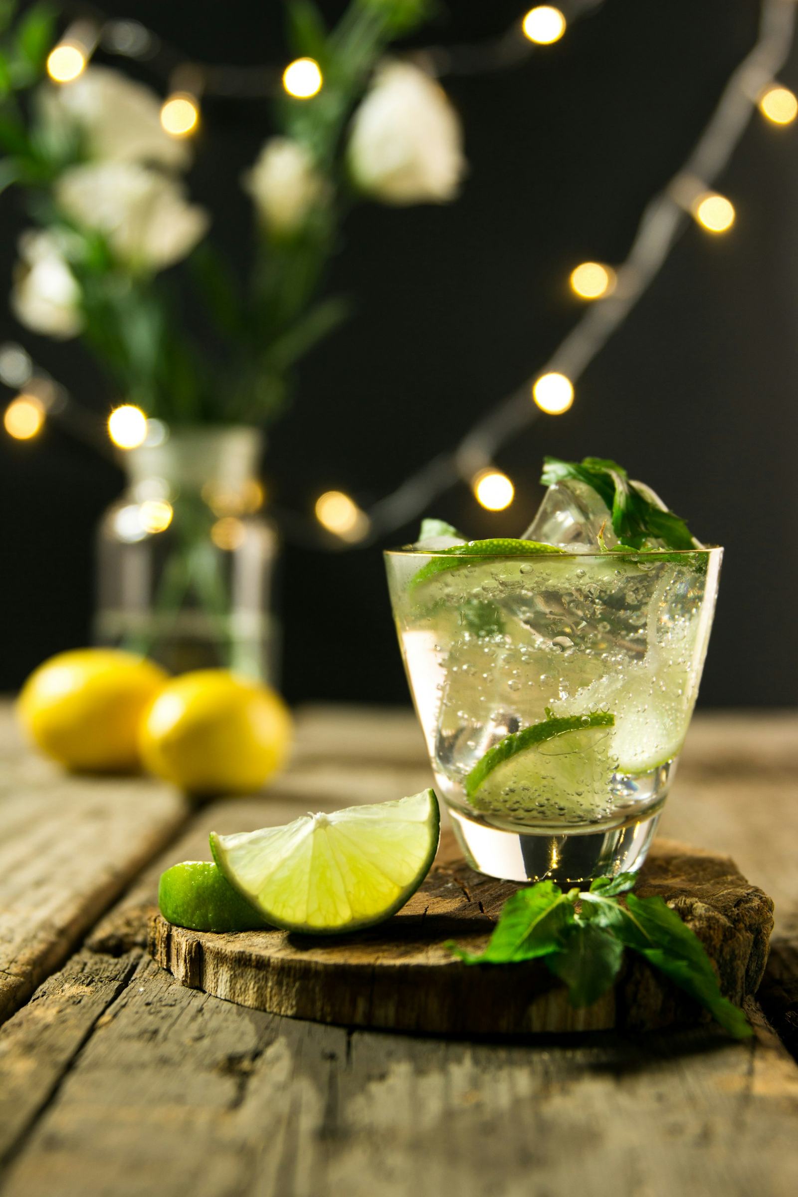 A tall mojito on a wooden table with fairy lights glowing softly behind it at a garden party