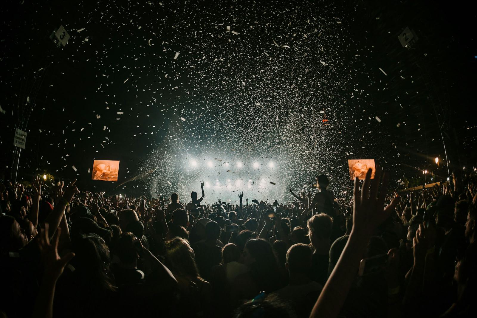 A packed night-time crowd lit by stage lights with confetti in the air